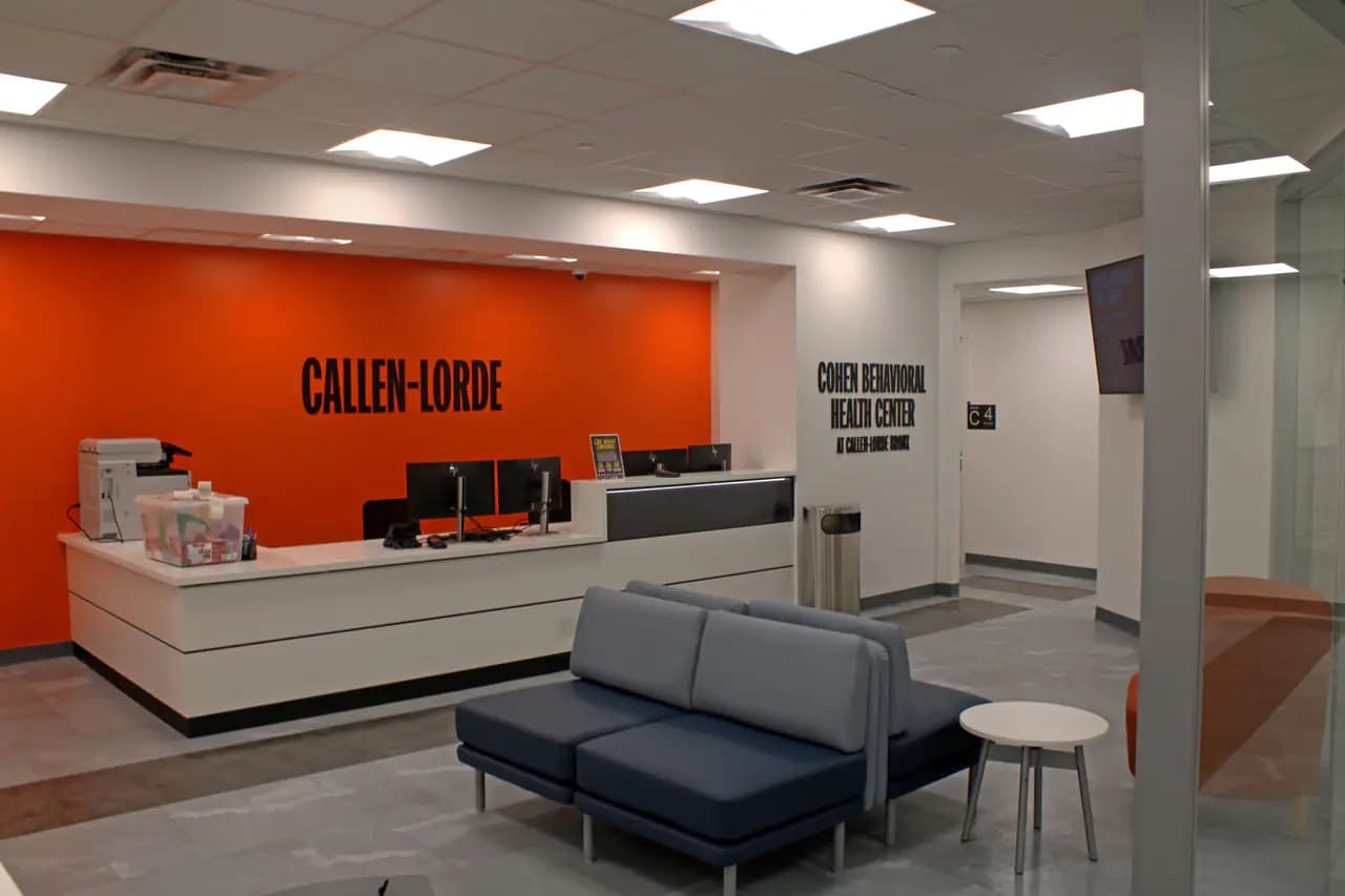 The reception desk and waiting area of Callen-Lorde's new Bronx clinic, with an orange wall bearing the Callen-Lorde name