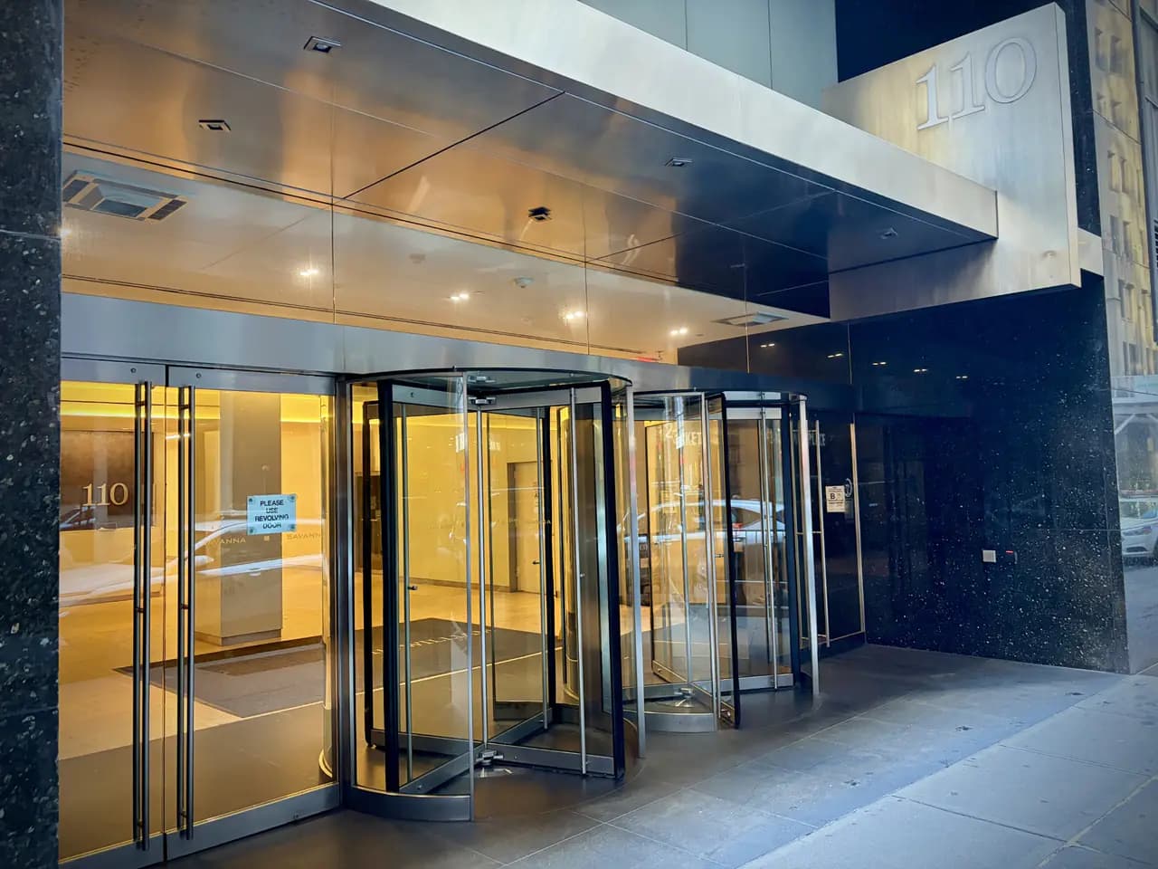 Glass revolving doors at the front entrance of 110 William Street in Lower Manhattan, with the number 110 above the doorway