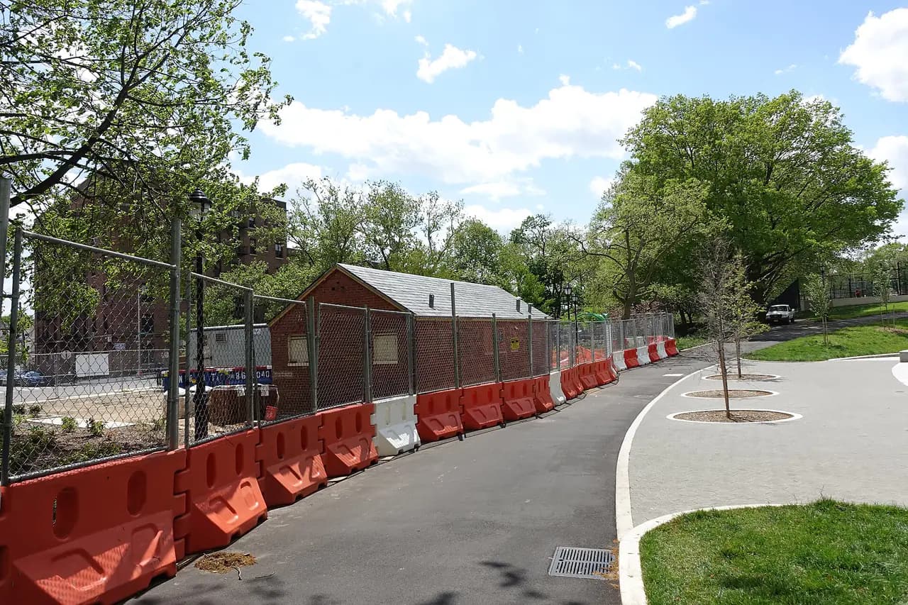A brick park comfort station behind a chain-link fence and orange barriers in Highland Park